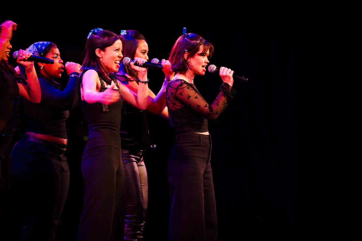 Julia Lebow singing with an ensemble under red stage lighting.